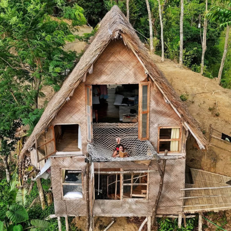 A woman sits on a treehouse balcony surrounded by lush forest greenery