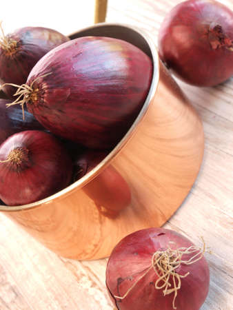 Red onions in a copper pan on a rustic wooden backgroundの写真素材