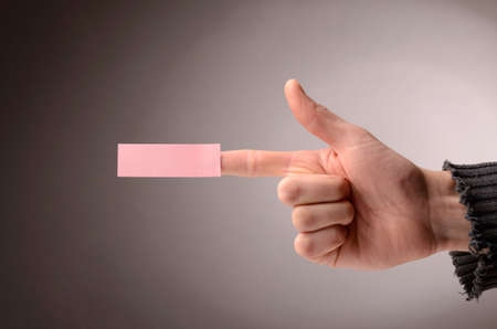 Male hand making a pistol with a sticky note on the index fingerの写真素材