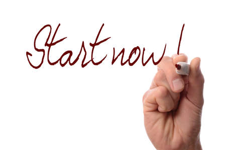 Hand with a red pen writing Start now! on a glass backgroundの写真素材