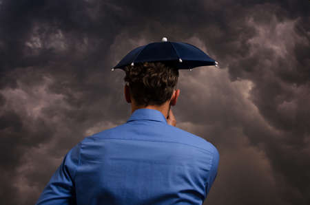 Business man with small umbrella in front of a heavy stormの写真素材