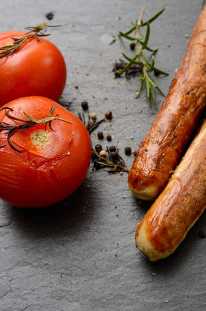 Grilled tomatoes and sausages on a dark slate backgroundの写真素材