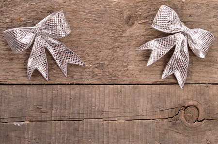 Two silver bows on a rustic wooden background with space for text or imageの写真素材