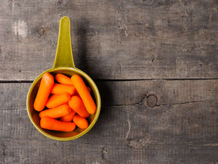 Small fresh carrots in a ceramic bowl on a rustic wooden table with space for textの写真素材