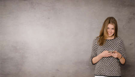 Happy female teenager with a mobile phone on a wall with space for text or imageの写真素材