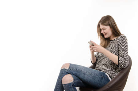 Young girl on a lounge chair writing with her cell phoneの写真素材