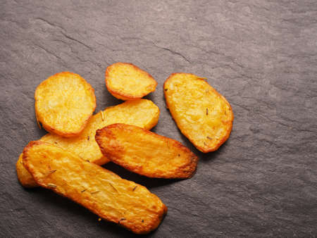 Roasted potato wedges with rosemary and thyme on a dark slate background with space for textの写真素材