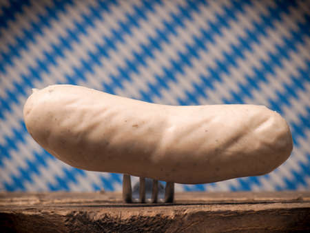 Bavarian veal sausage on a fork in front of a Bavarian flag, selective focus on the sausageの写真素材