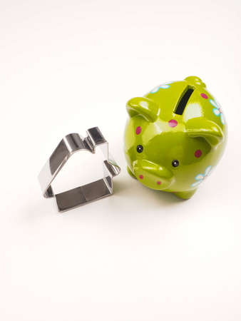 Green ceramic piggy bank with a steel house shape on a bright tableの写真素材