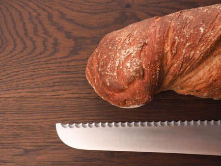 Delicious organic bread with a big bread knife on a wooden table with space for textの写真素材