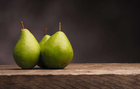 Three delicious green pears on an old wooden table with space for textの写真素材