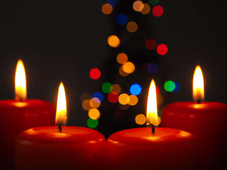 Four burning Advent candles with blurred lights background of a Christmas treeの写真素材