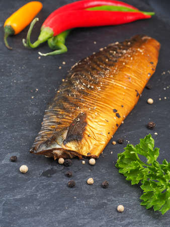 Smoked mackerel with pepper and cooking ingredients on a dark slate plate in a kitchenの写真素材