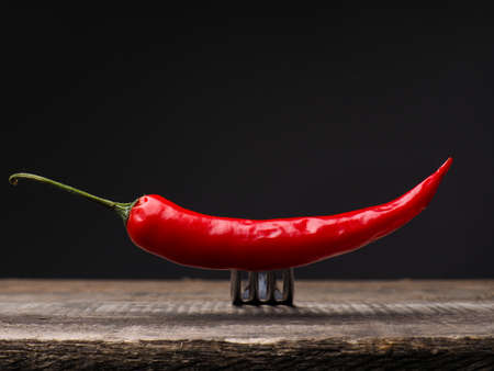 Stainless steel fork with a red chili on a rustic wooden tableの写真素材
