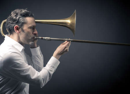 Musician with an old used trombone on a dark backgroundの写真素材