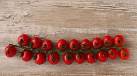 Branch of fresh cherry tomatoes on a wooden background with space for textの写真素材