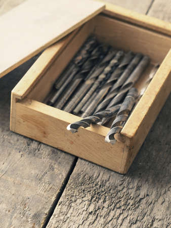Old used drills in a wooden box on a wooden surfaceの写真素材