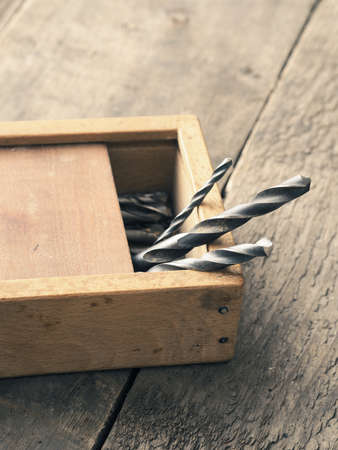 Old used drills in a wooden box on a workbenchの写真素材