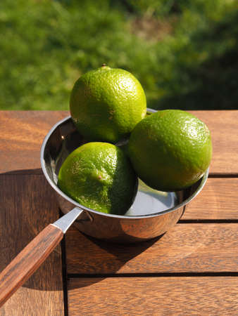 Three fresh organic lime fruits in a steel bowl on a wooden garden tableの写真素材