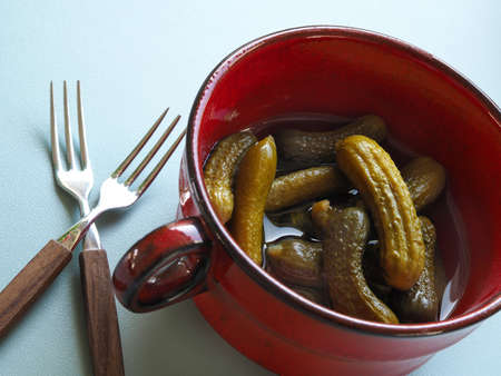 Gherkins in a rustic red ceramic bowl on a modern kitchen tableの写真素材