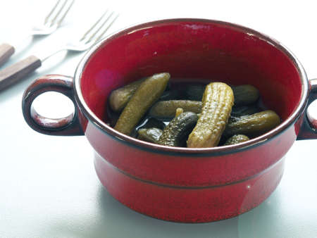 Gherkins in a rustic red ceramic bowl on a modern kitchen tableの写真素材