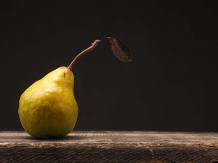 One organic pear on a rustic wooden kitchen table space for text on the rightの写真素材