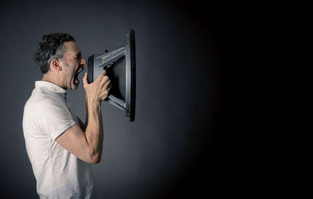 Young man holding a big speaker, speaking loud concept on a dark studio background with space for...