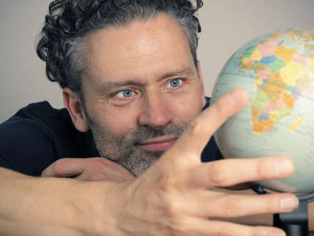 Handsome man looking a small globe to find the next travel destination