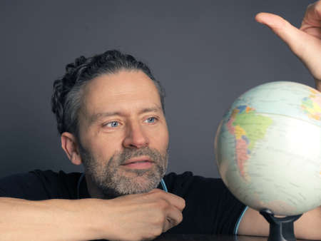 Handsome man looking at a small globe to find the next travel destination
