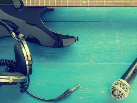 Old vintage headphones and guitar on a rustic blue wooden plank with space for text