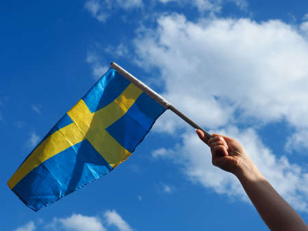 Female hand waving with the Swedish flag on a blue summer skyの写真素材