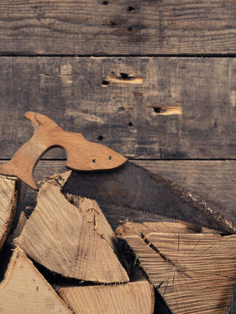 Pile of beech fire wood with an old and rusty saw, space for text on wooden wallの写真素材