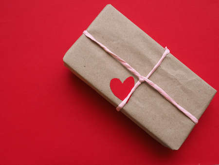 Gift box with a red heart shape on a red table cloth with space for textの写真素材