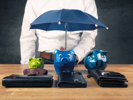 Businessman holding a small blue umbrella, protection or security concept image, protect your savingsの写真素材