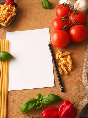 Pasta or Italian food concept background with an empty paper sheet and pencil on a wooden tableの写真素材