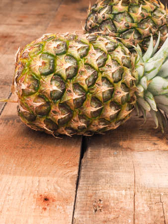 Organic pineapples on a rustic wooden kitchen table with space for textの写真素材