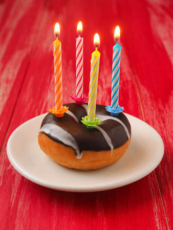 Colorful birthday candles with a donut on a red wooden tableの写真素材