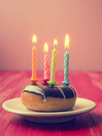 Colorful birthday candles with a donut on a red wooden table, vintage color stylizedの写真素材