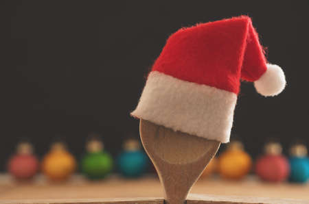 Wooden cooking spoon with hat of Santa on a chalkboard with colorful Christmas baubles