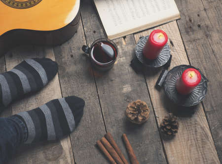Young man sitting on a rustic wooden flooring with his guitar and mulled wineの写真素材