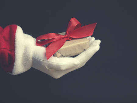 Hand of Santa with gift box on a dark background, modern flat tone stylized Christmas conceptの写真素材