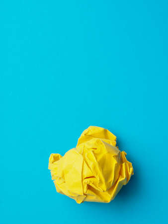 Crumpled yellow paper ball on a blue background with space for your text or imageの写真素材