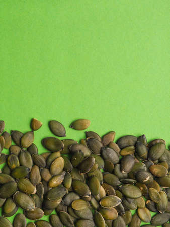 Organic pumpkin seeds on a green background with space for text or image, healthy food concept の写真素材