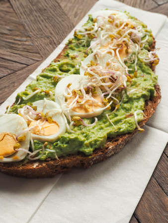 Tasty organic bread with Avocado cream and eggs on a rustic wooden tableの写真素材