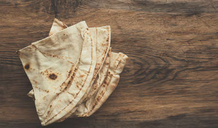 Stacked flatbread on a rustic wooden kitchen table, view from above with space for text 