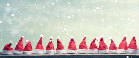 Hats of Santa in a row on a rustic wooden table, panoramic view