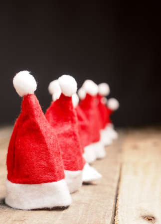 Many hats of Santa in a row on a rustic wooden table with space for textの写真素材