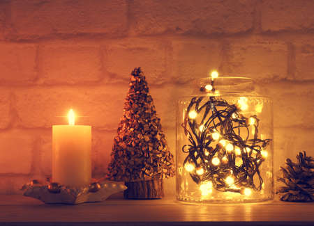 Magical Christmas background with a jar filled with christmas lights and a burning candle on a tableの写真素材