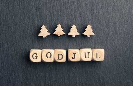 God Jul, Scandinavian Merry Christmas on small wooden dices with four little Christmas tree shapes on dark slateの写真素材