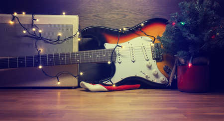 Old used vintage guitar with Christmas lights on a wooden table and space for text